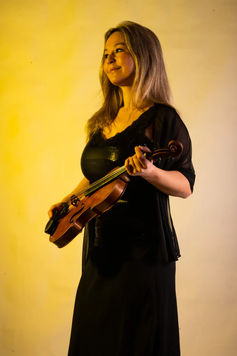 Violinist in black with her violin, warm yellow backdrop — Münchner Symphoniker, musician portrait photography by Janina Laszlo, Munich