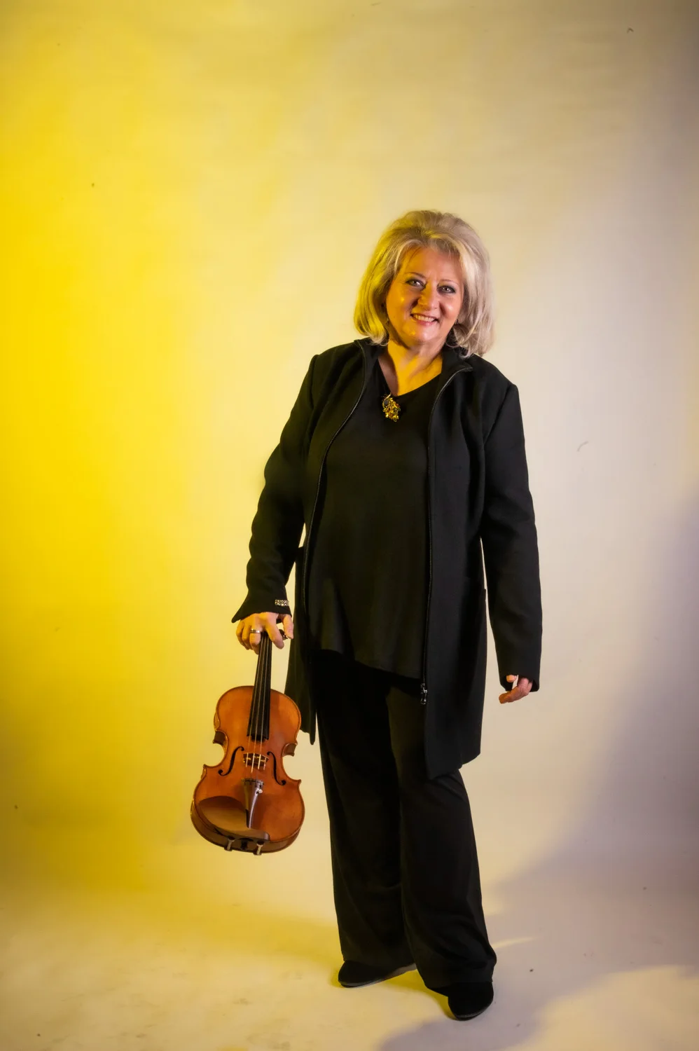 Violinist with grey hair holding his violin, warm yellow backdrop — Münchner Symphoniker, musician portrait photography by Janina Laszlo, Munich