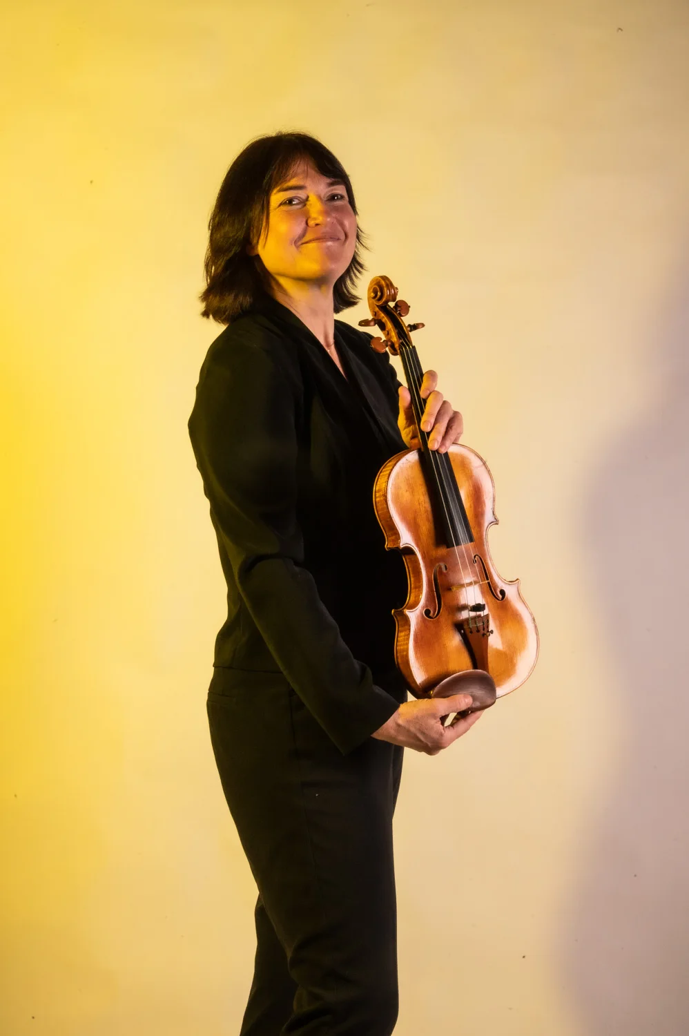 Violinist in profile with her violin, warm yellow backdrop — Münchner Symphoniker, musician portrait photography by Janina Laszlo, Munich