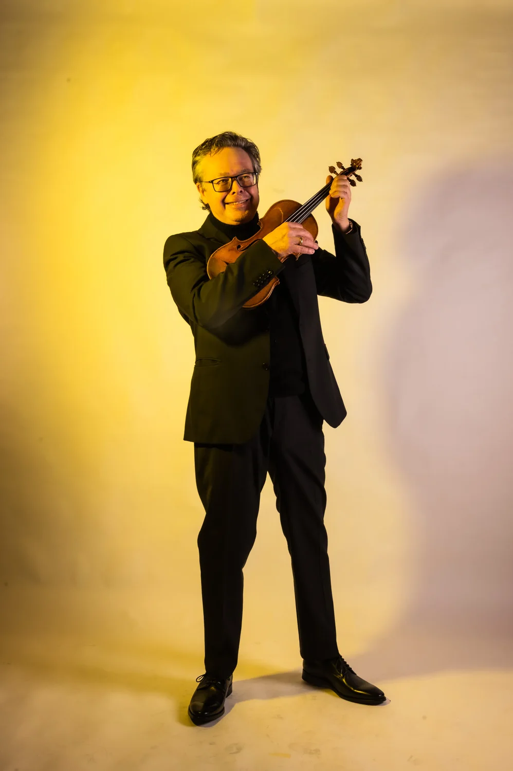 Violinist playing with a smile, warm yellow backdrop — Münchner Symphoniker, musician portrait photography by Janina Laszlo, Munich