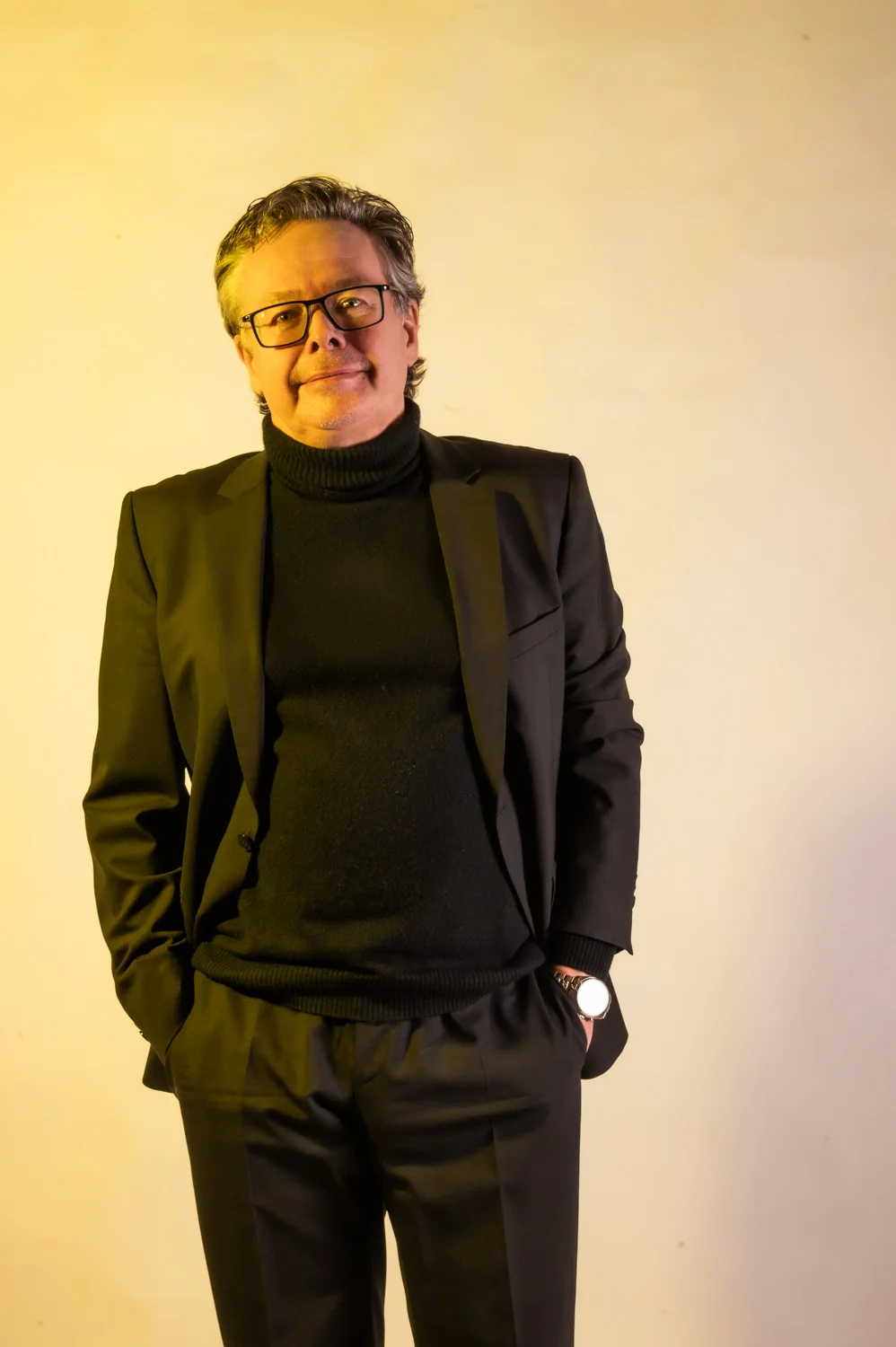 Musician with glasses in a black jacket, warm yellow backdrop — Münchner Symphoniker, musician portrait photography by Janina Laszlo, Munich