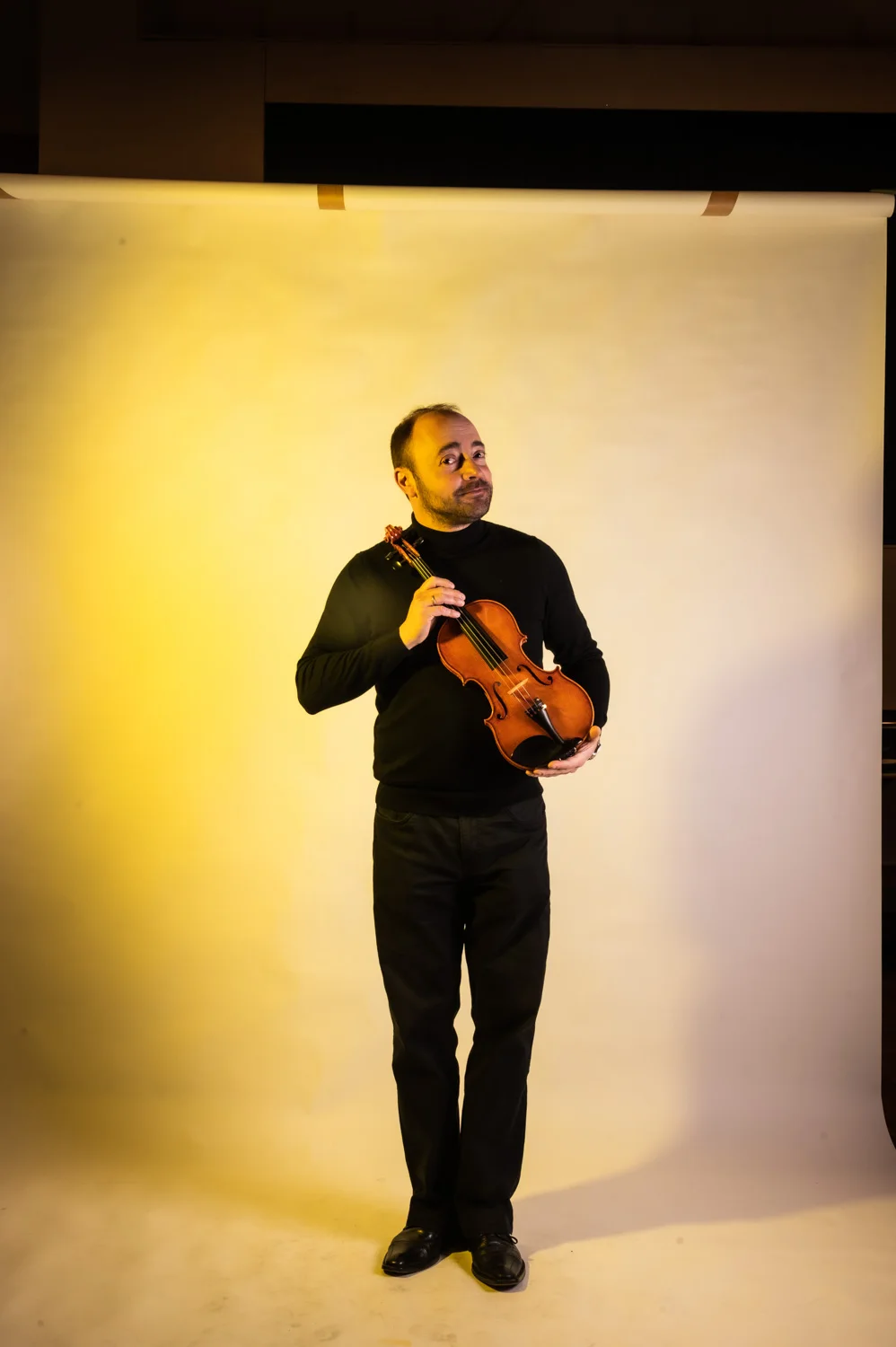 Violinist standing in a wide frame, warm yellow backdrop — Münchner Symphoniker, musician portrait photography by Janina Laszlo, Munich