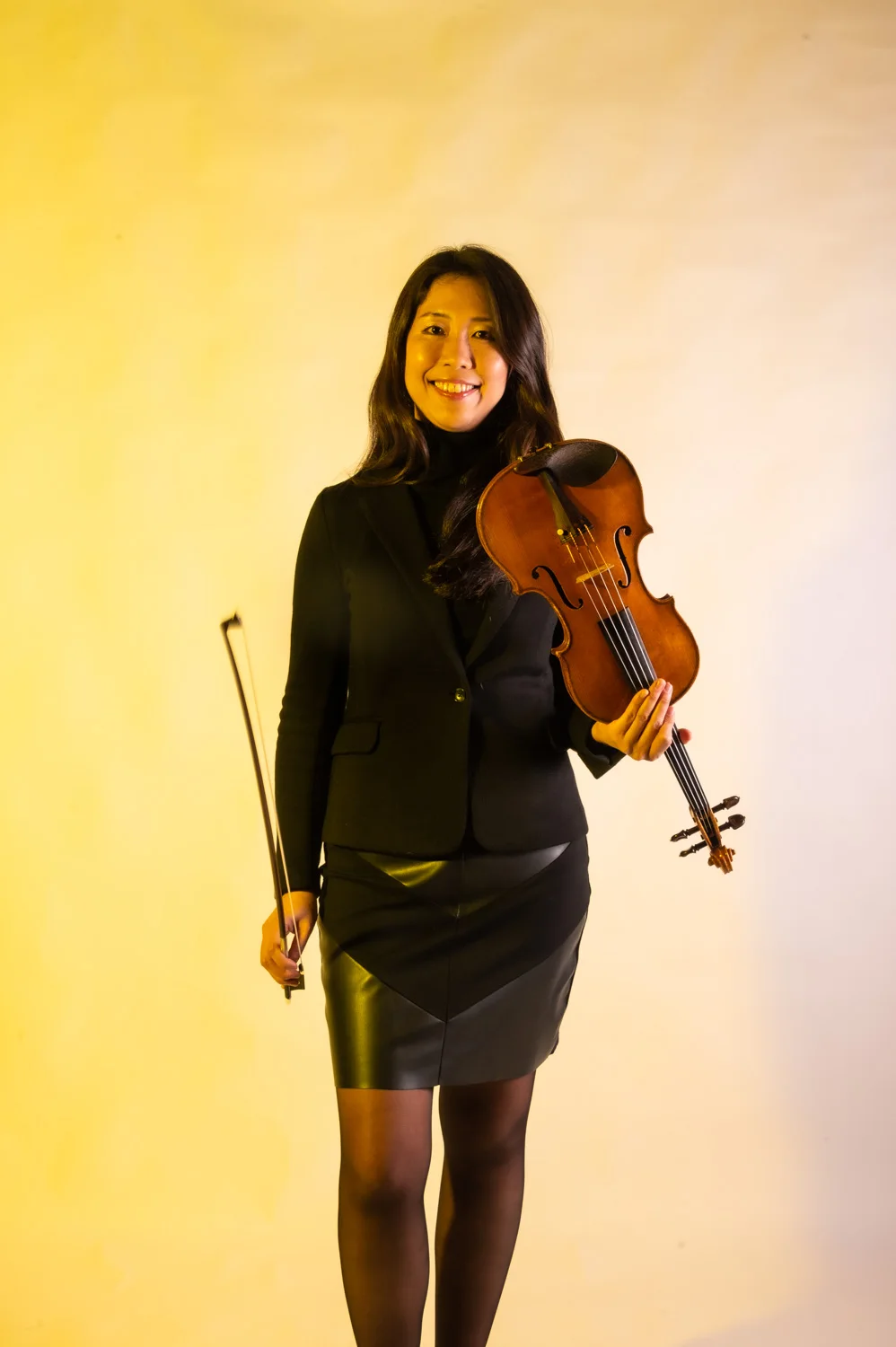 Violinist with long dark hair playing, warm yellow backdrop — Münchner Symphoniker, musician portrait photography by Janina Laszlo, Munich