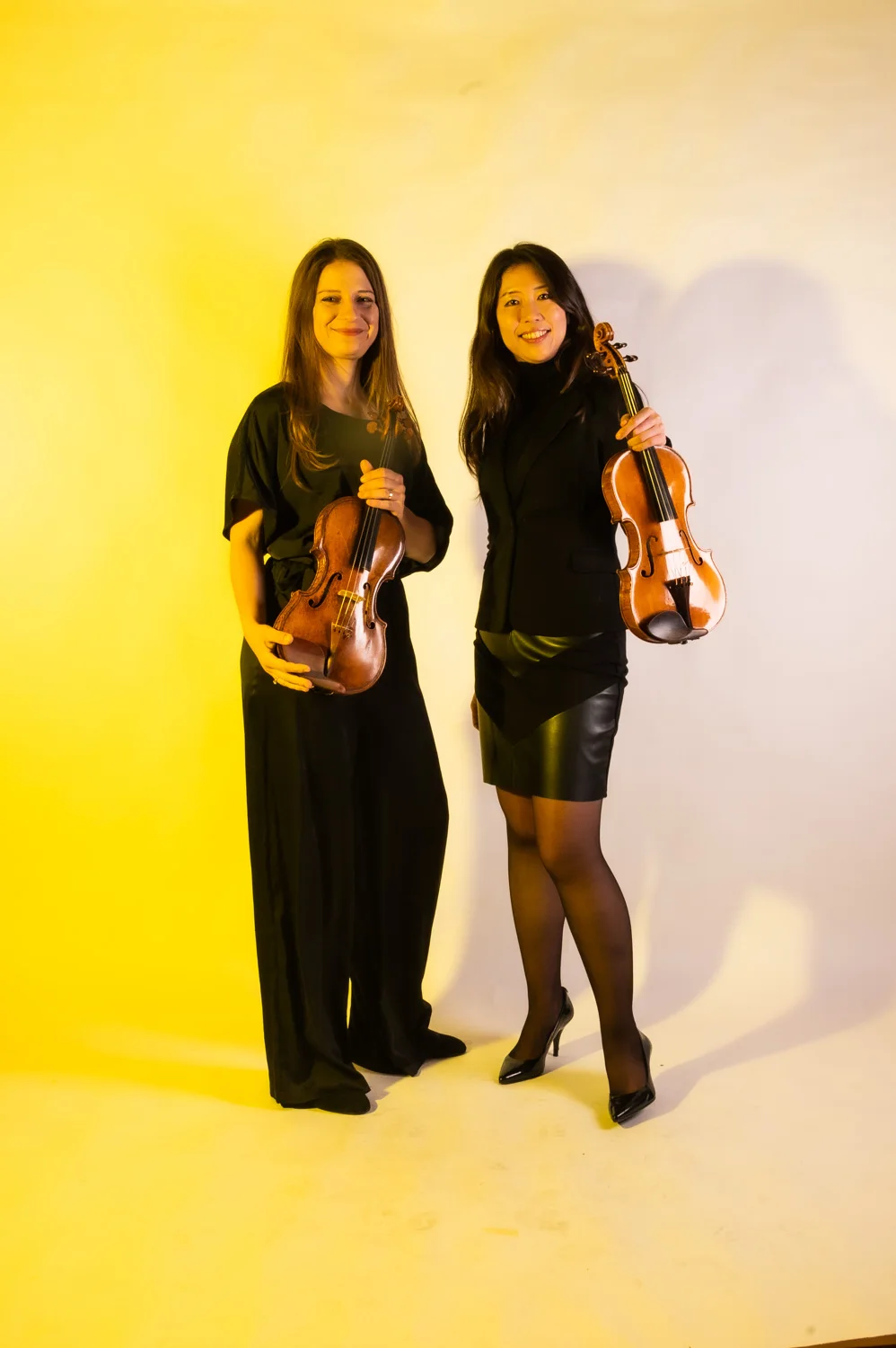 Two violinists side by side, warm yellow backdrop — Münchner Symphoniker, musician portrait photography by Janina Laszlo, Munich