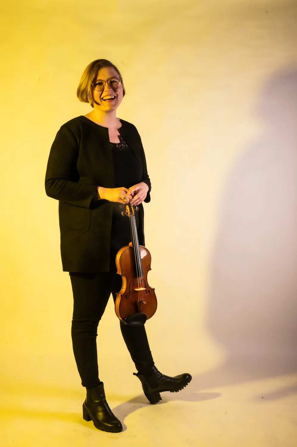 Violinist standing with her bow, warm yellow backdrop — Münchner Symphoniker, musician portrait photography by Janina Laszlo, Munich
