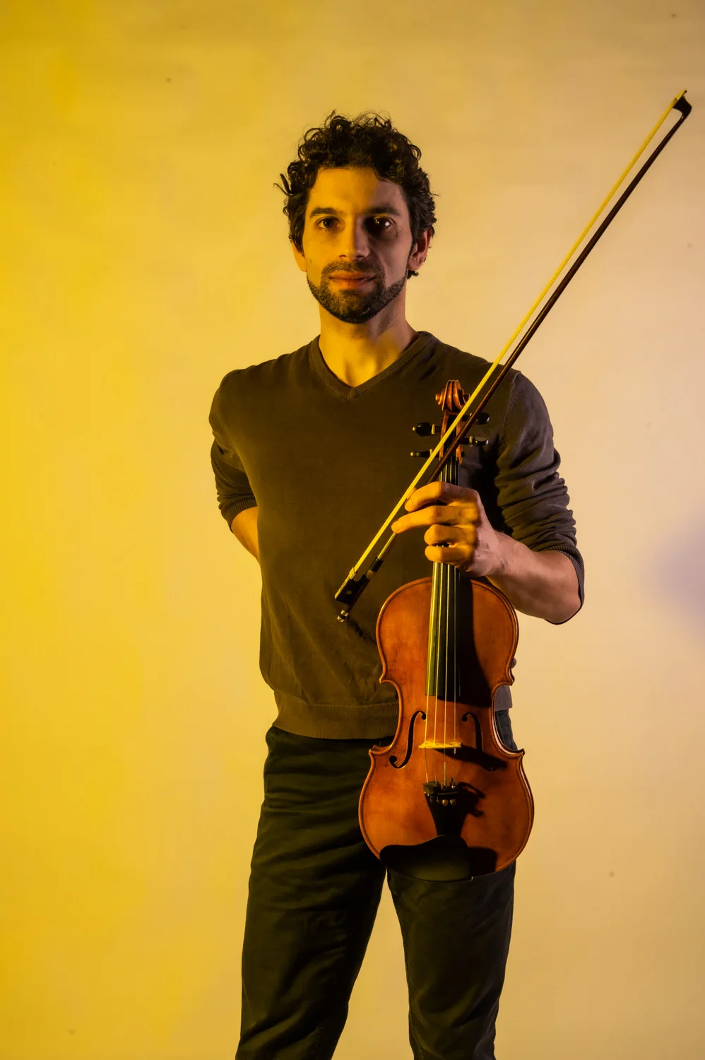 Violinist with a bow raised, warm yellow backdrop — Münchner Symphoniker, musician portrait photography by Janina Laszlo, Munich