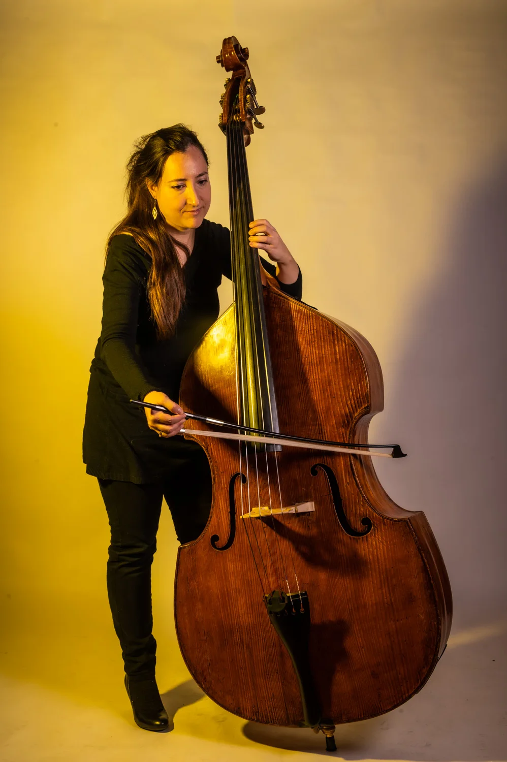 Double bassist leaning on her bass, warm yellow backdrop — Münchner Symphoniker, musician portrait photography by Janina Laszlo, Munich