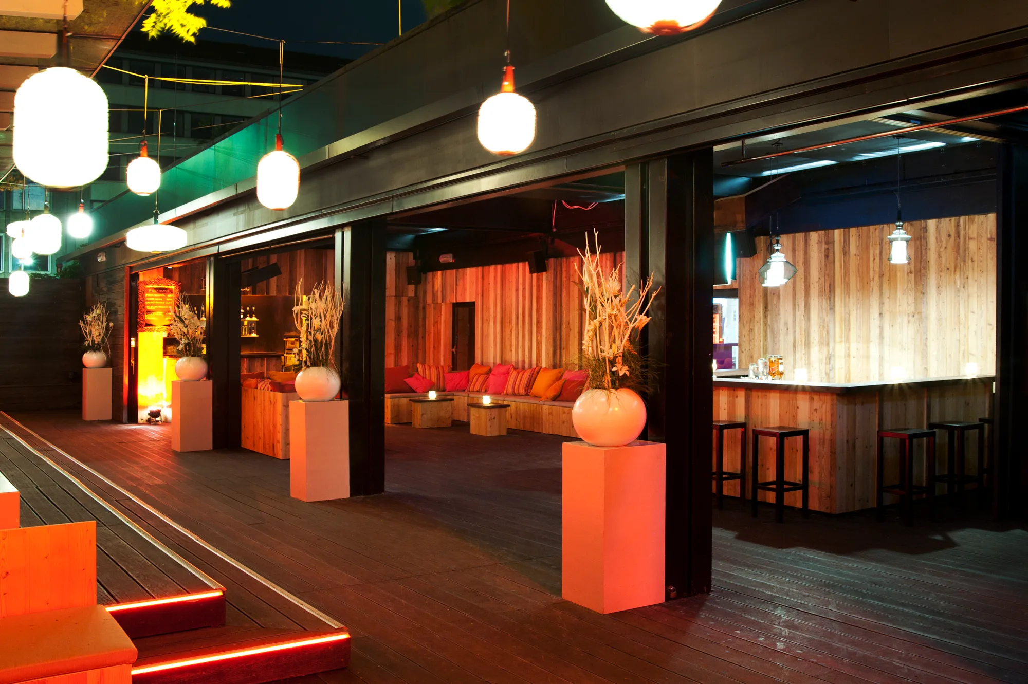 Night terrace with glowing paper lanterns, white floral arrangements on pedestals and an open bar clad in rough wood — Pacha Munich, interior and architectural photography by Janina Laszlo, Munich