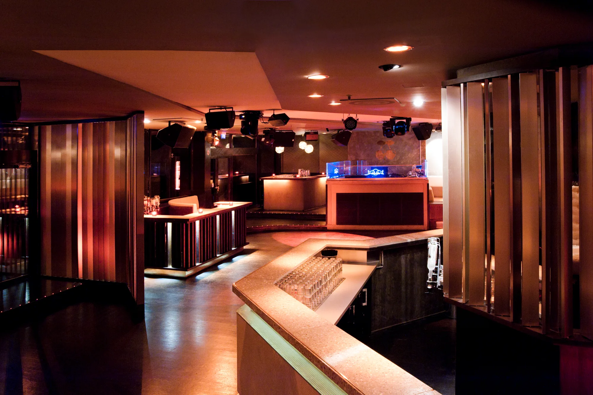 Club floor with bronze vertical lamellas, terrazzo bar counter and illuminated DJ booth — Pacha Munich, interior and architectural photography by Janina Laszlo, Munich