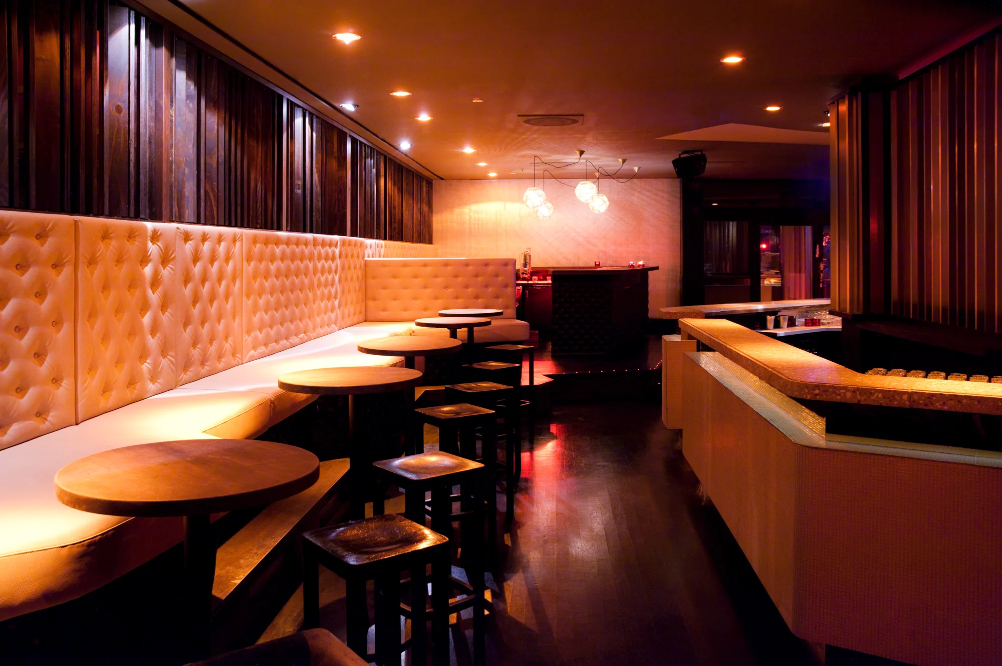 Long tufted leather banquette with round wooden tables and stools in warm amber light — Pacha Munich, interior and architectural photography by Janina Laszlo, Munich