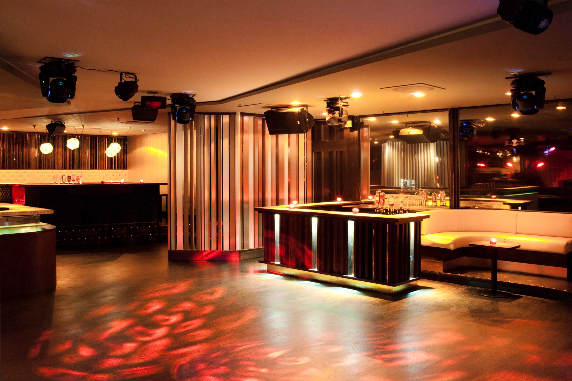 Dance floor with red light projections, a bronze lamella column and a timber-slatted bar with backlit joints — Pacha Munich, interior and architectural photography by Janina Laszlo, Munich