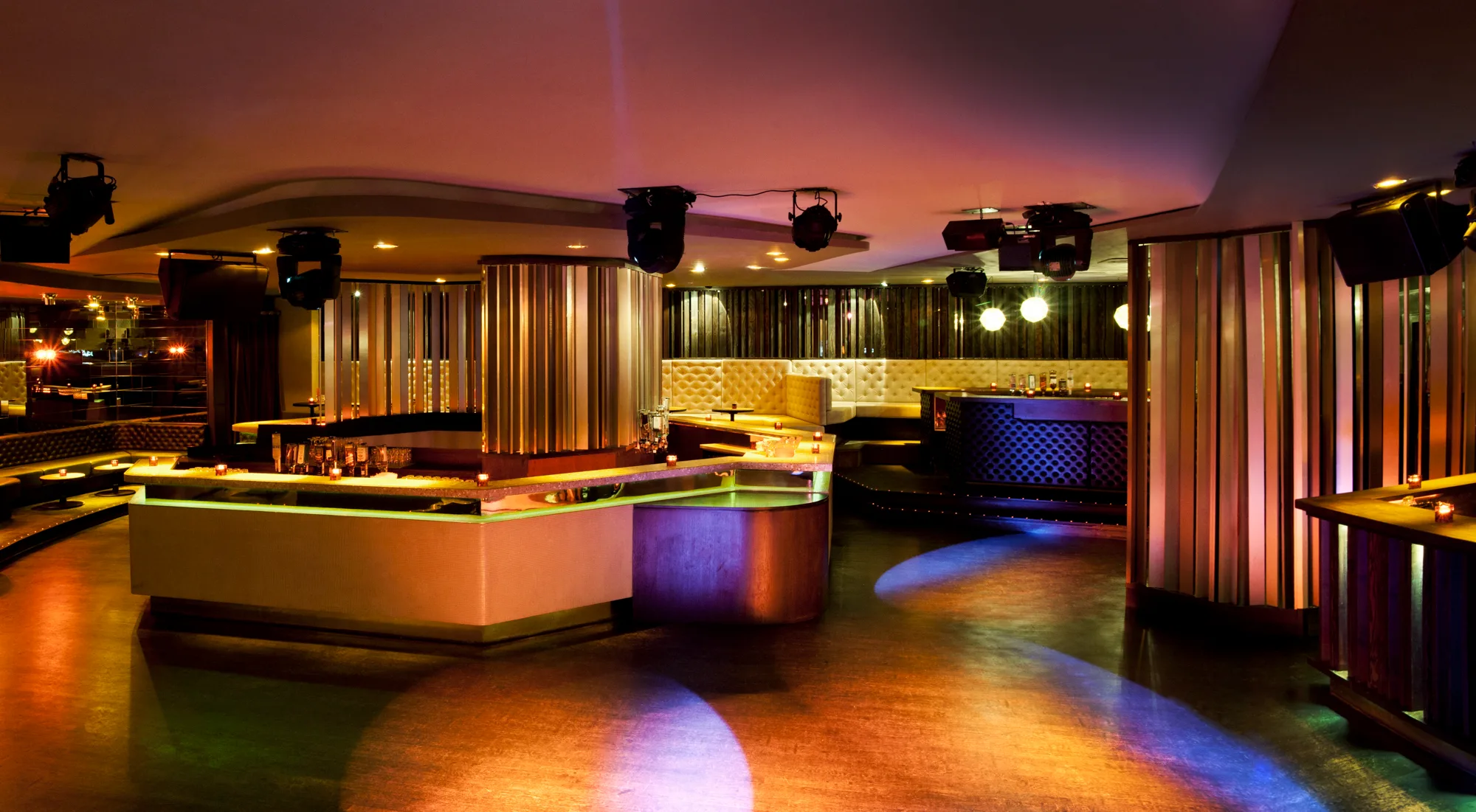 Panoramic view of the main room with island bar, lamella columns and coloured light pools on the wooden floor — Pacha Munich, interior and architectural photography by Janina Laszlo, Munich