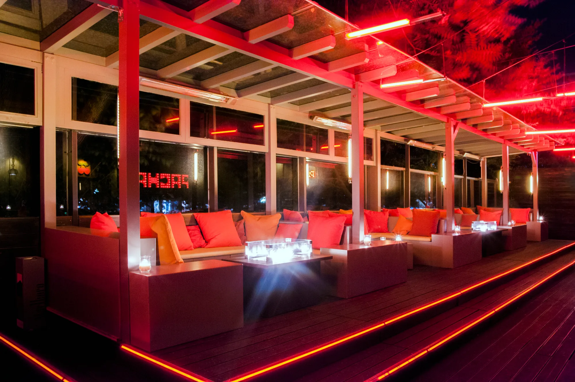 Covered terrace lounge with orange cushions, glass fire tables and red neon lines along the steps — Pacha Munich, interior and architectural photography by Janina Laszlo, Munich