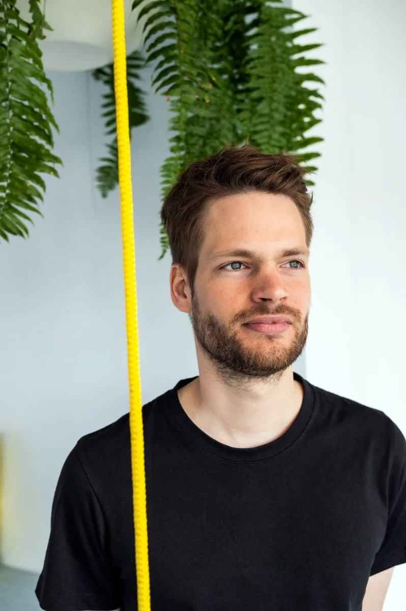 Personio co-founder in a black T-shirt beside hanging ferns and a yellow rope, Munich office — Personio, corporate photography by Janina Laszlo
