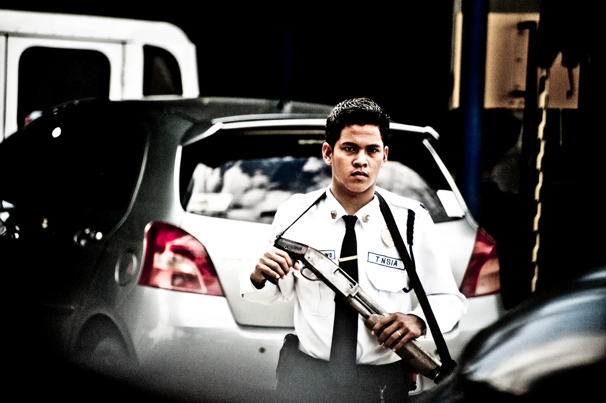 Security guard in white uniform holding a pump-action shotgun in a car park — Palawan, Philippines, documentary and travel photography by Janina Laszlo