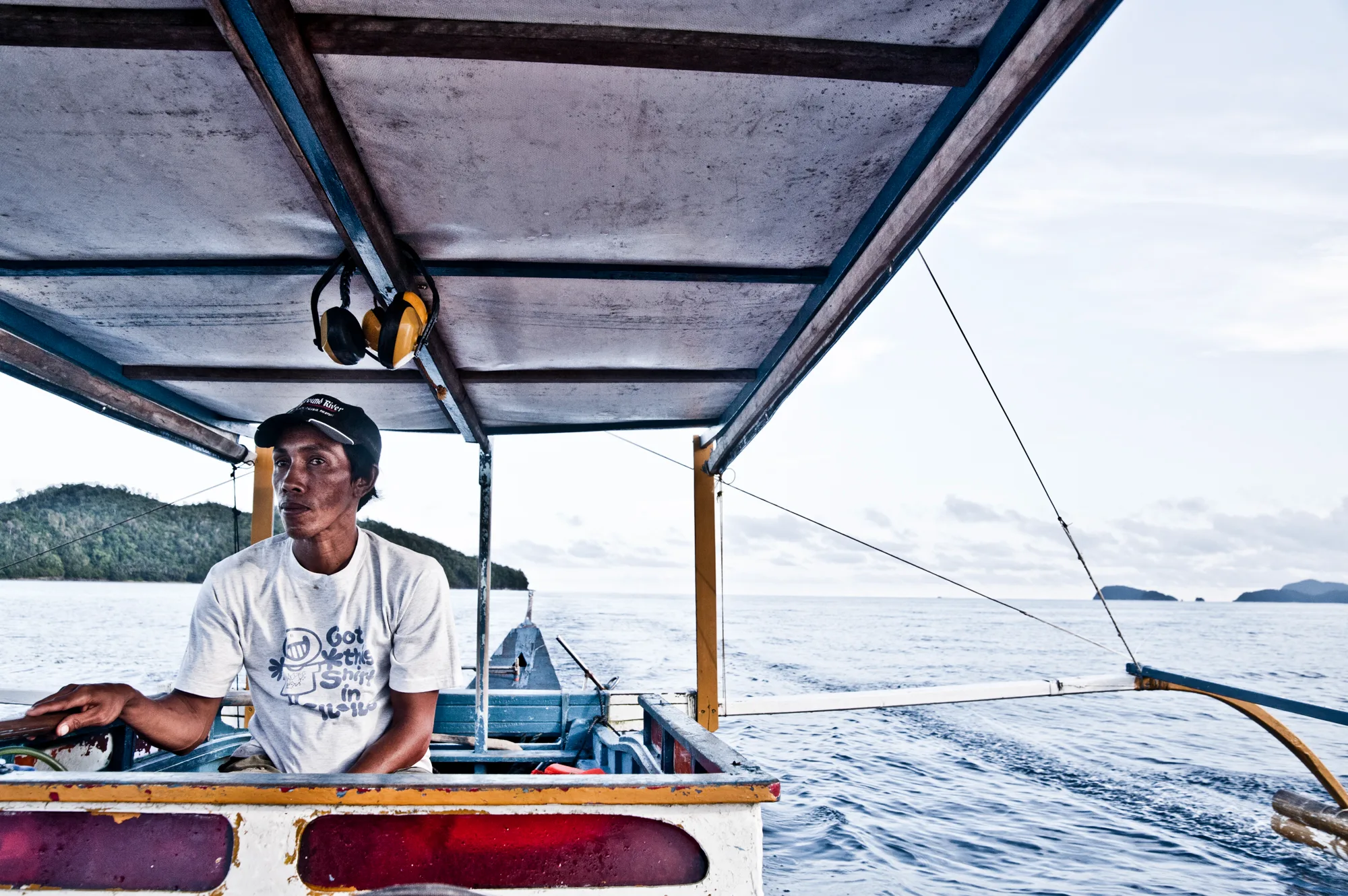 Boatman steering a bangka outrigger boat past green islands — Palawan, Philippines, documentary and travel photography by Janina Laszlo