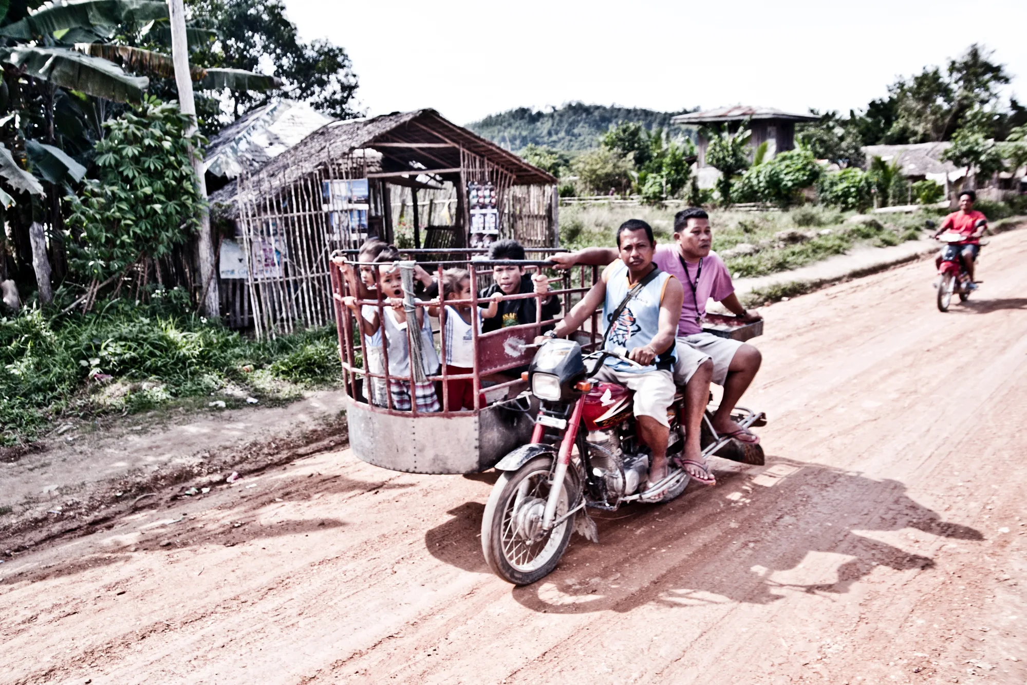Children riding in a metal sidecar of a motorcycle tricycle on a red dirt road — Palawan, Philippines, documentary and travel photography by Janina Laszlo