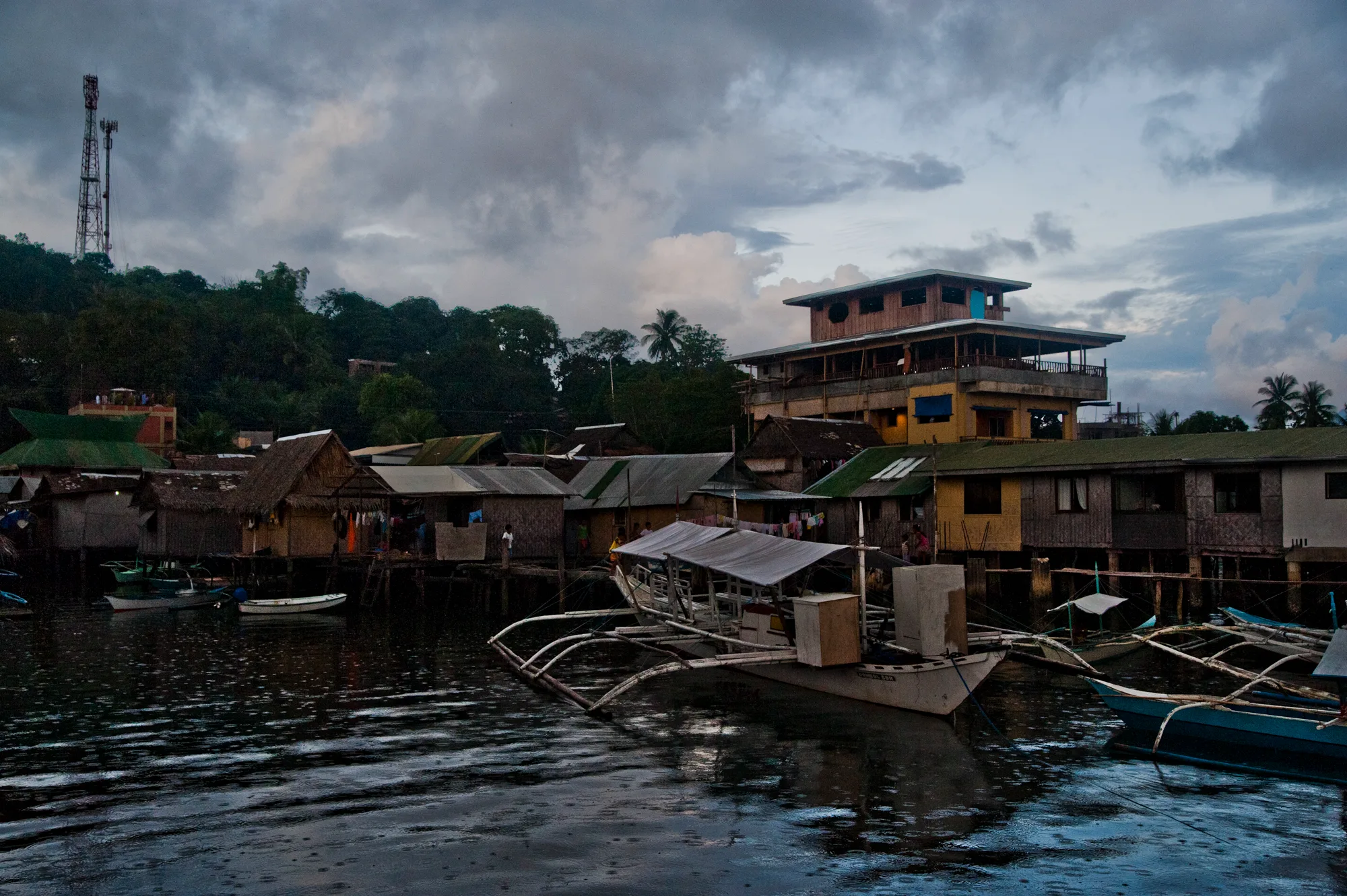 Stilt houses and bangka boats on the waterfront at dusk in the rain — Palawan, Philippines, documentary and travel photography by Janina Laszlo