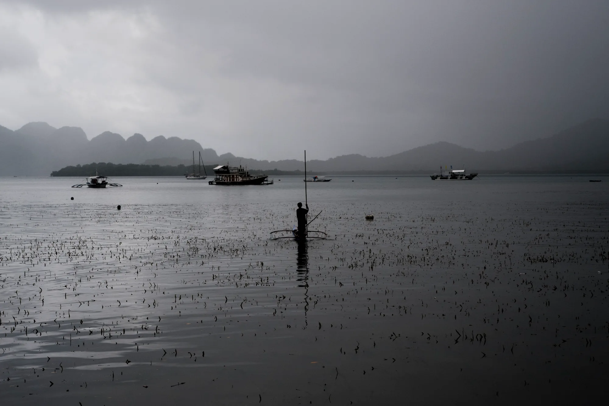 Fisherman poling a small outrigger boat across a misty bay below karst mountains, El Nido — Palawan, Philippines, documentary and travel photography by Janina Laszlo