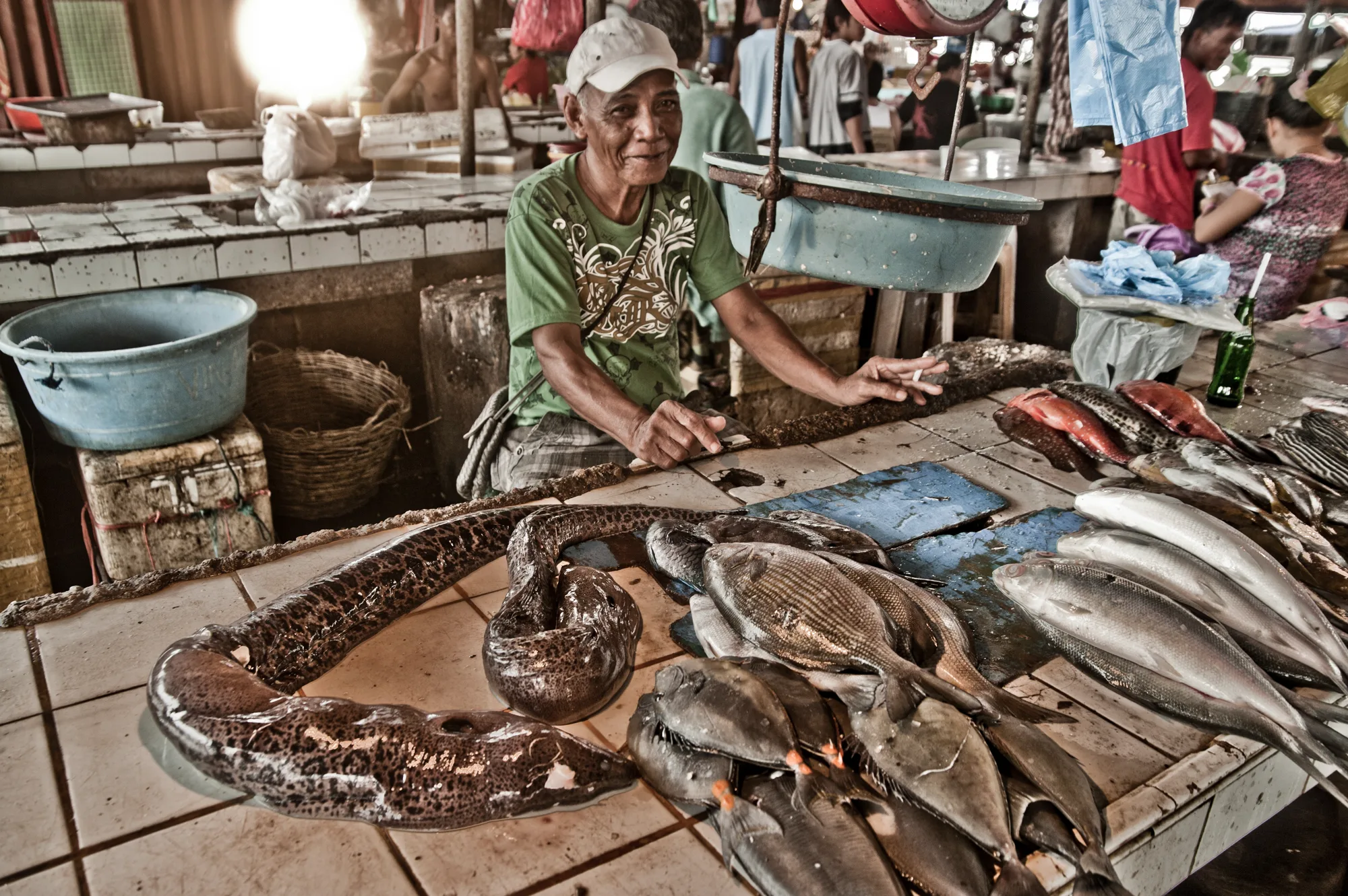 Smiling fish vendor with moray eels and reef fish on a tiled market counter — Palawan, Philippines, documentary and travel photography by Janina Laszlo