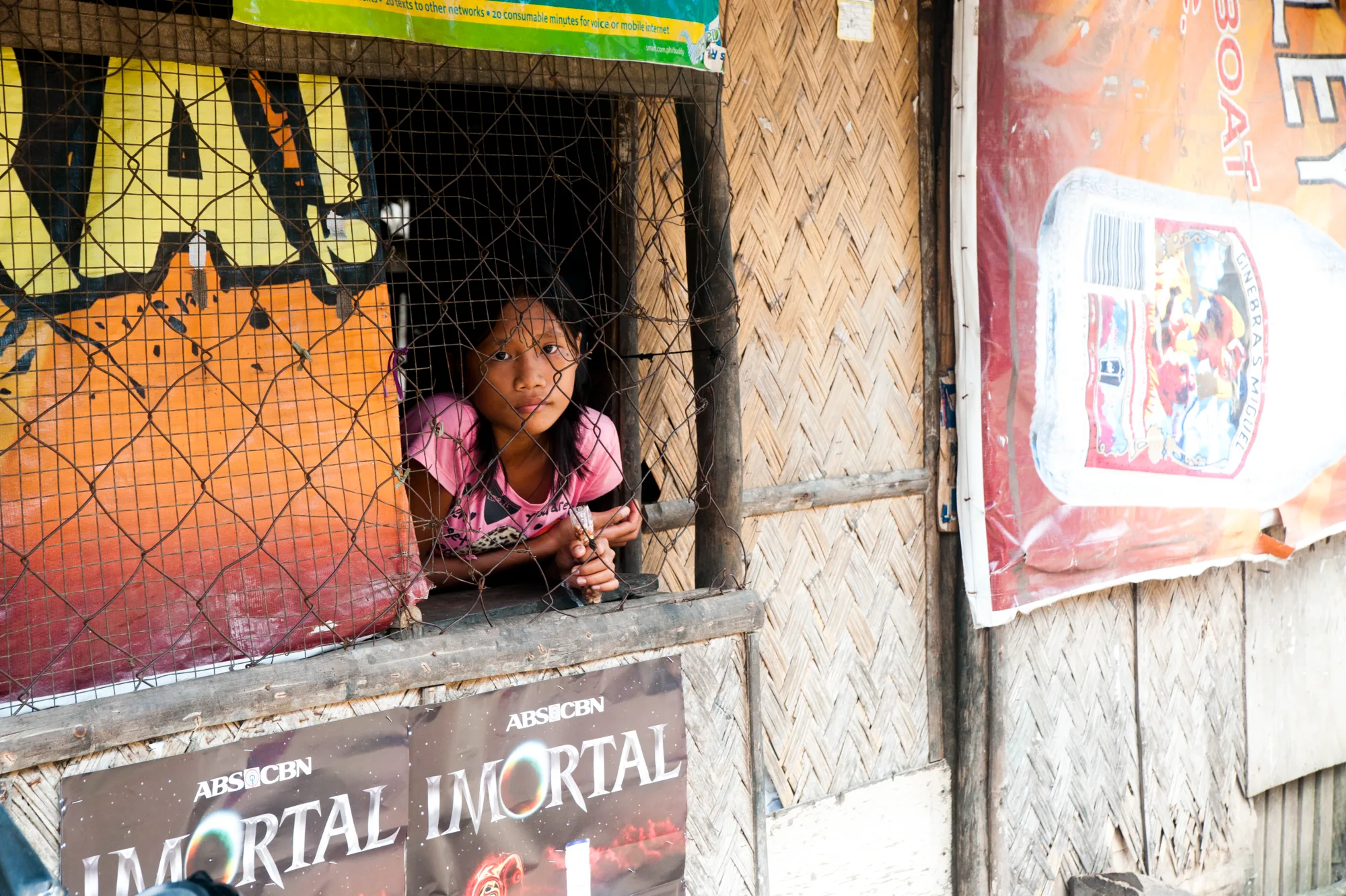 Girl looking through the chicken-wire window of a bamboo shop — Palawan, Philippines, documentary and travel photography by Janina Laszlo