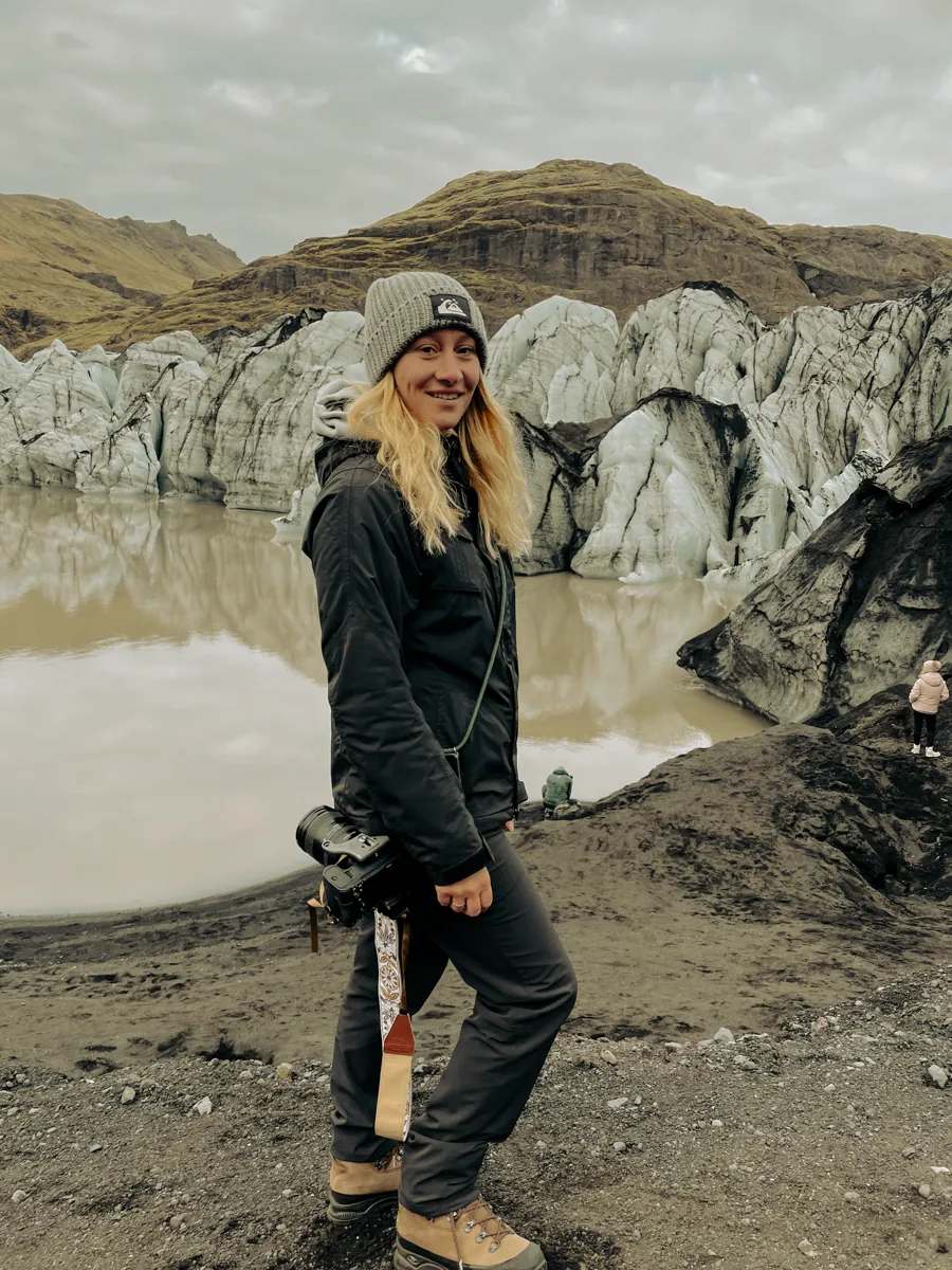 Photographer Janina Laszlo with her camera in front of a glacier lagoon in Iceland — portrait of the German commercial and editorial photographer on an international production