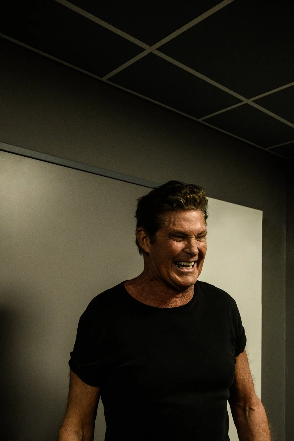 David Hasselhoff in a black T-shirt laughing in a dark corridor — behind-the-scenes photography during a concert appearance, by German photographer Janina Laszlo