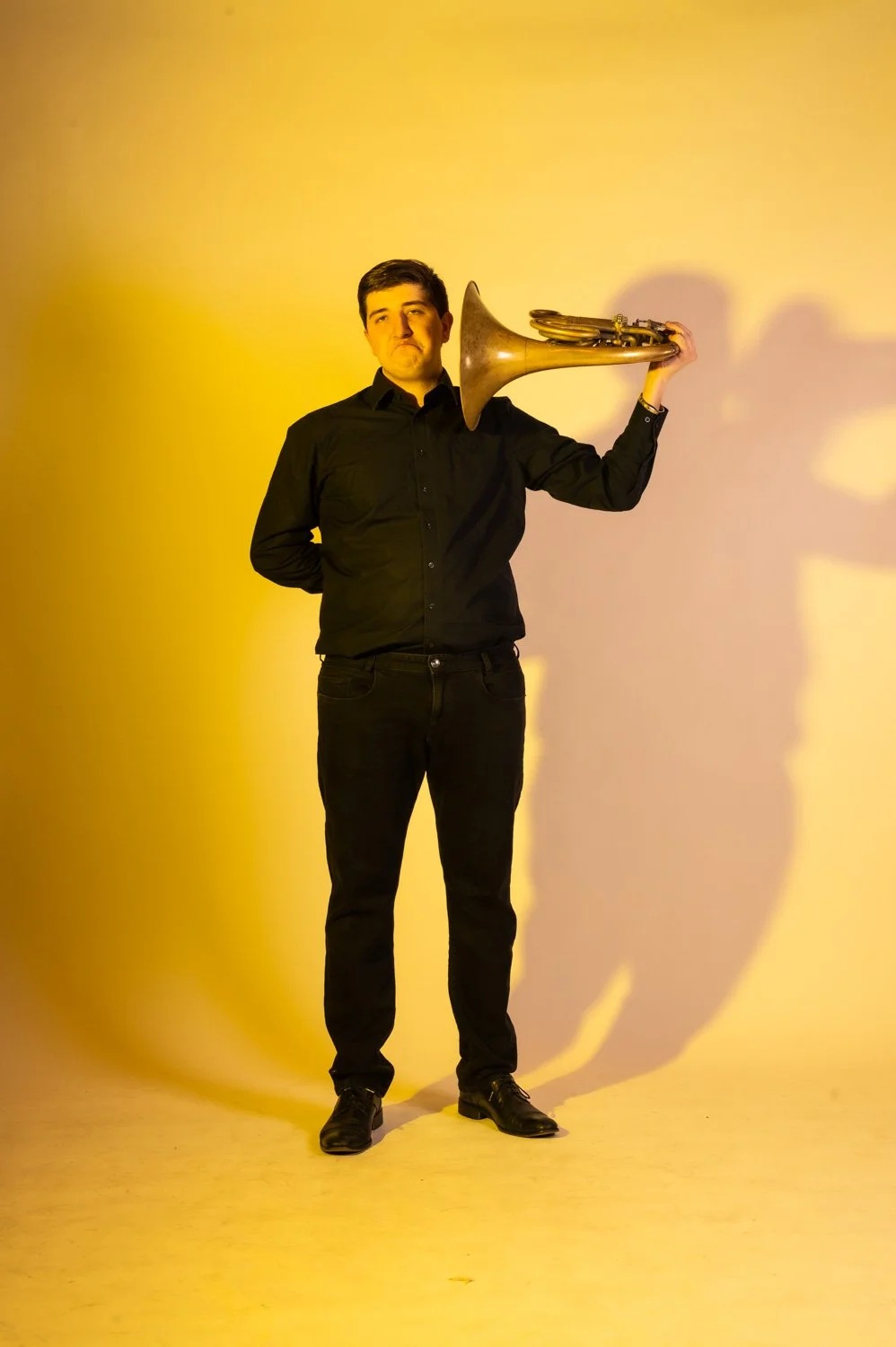 Trumpeter of the Münchner Symphoniker with his trumpet on his shoulder, yellow backdrop — portrait by Janina Laszlo, portrait photographer in Munich