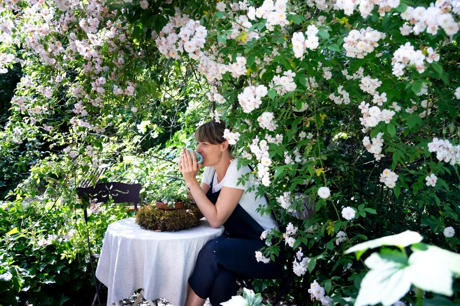 Sarah Stiller sitting at a garden table among white roses — My Cottage Garden rose garden, Sarah Stiller — campaign photography by Janina Laszlo, Munich