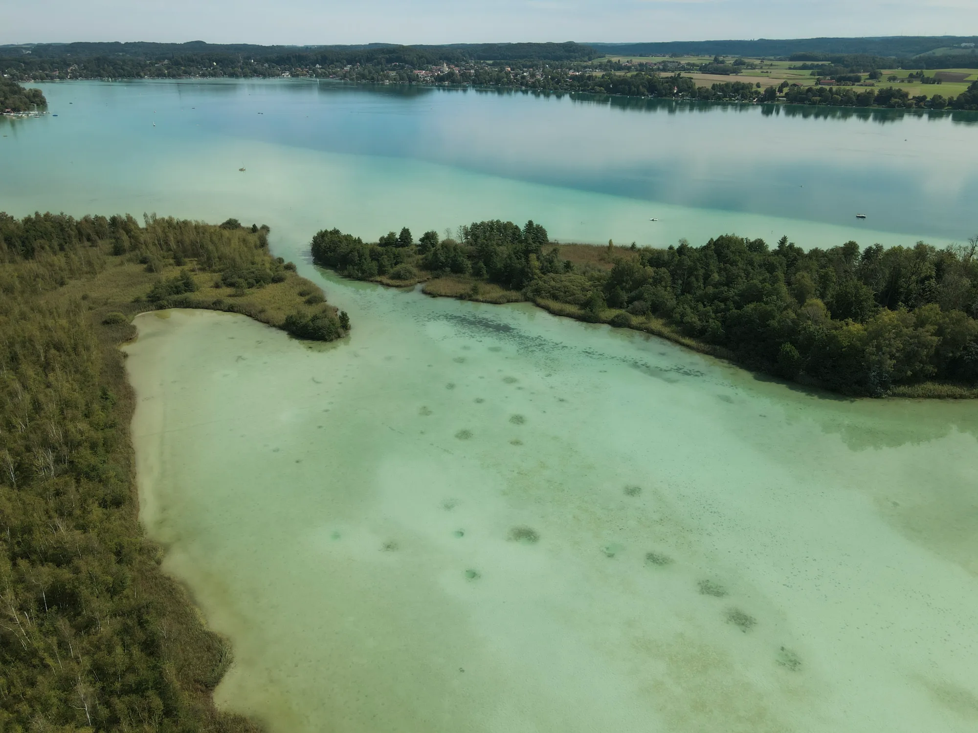 Aerial view of a turquoise shallow lake bay with wooded peninsulas and a lakeside village beyond over the Wörthsee — Fünfseenland for SEEMAGAZIN, editorial travel and landscape photography by Janina Laszlo, Munich