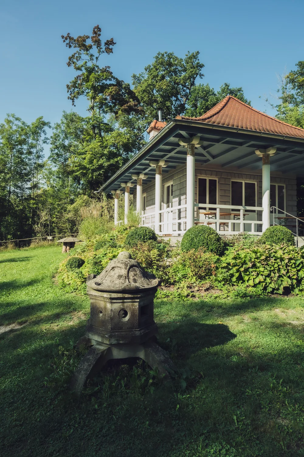 Garden pavilion with white columns and a tiled roof behind a historic stone lantern in the Schacky-Park in Dießen am Ammersee — Fünfseenland for SEEMAGAZIN, editorial travel and landscape photography by Janina Laszlo, Munich