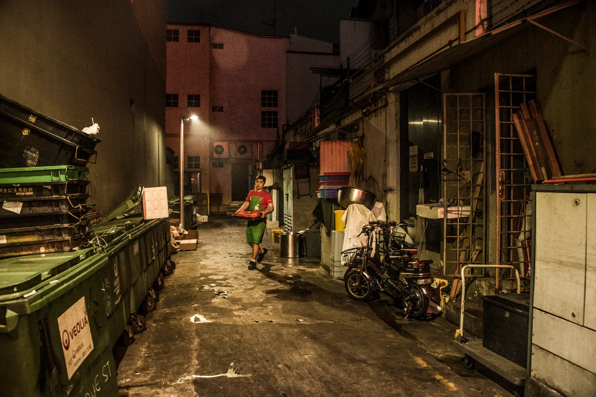 Kitchen worker carrying a tray through a back alley at night — Singapore, architecture and travel photography by Janina Laszlo