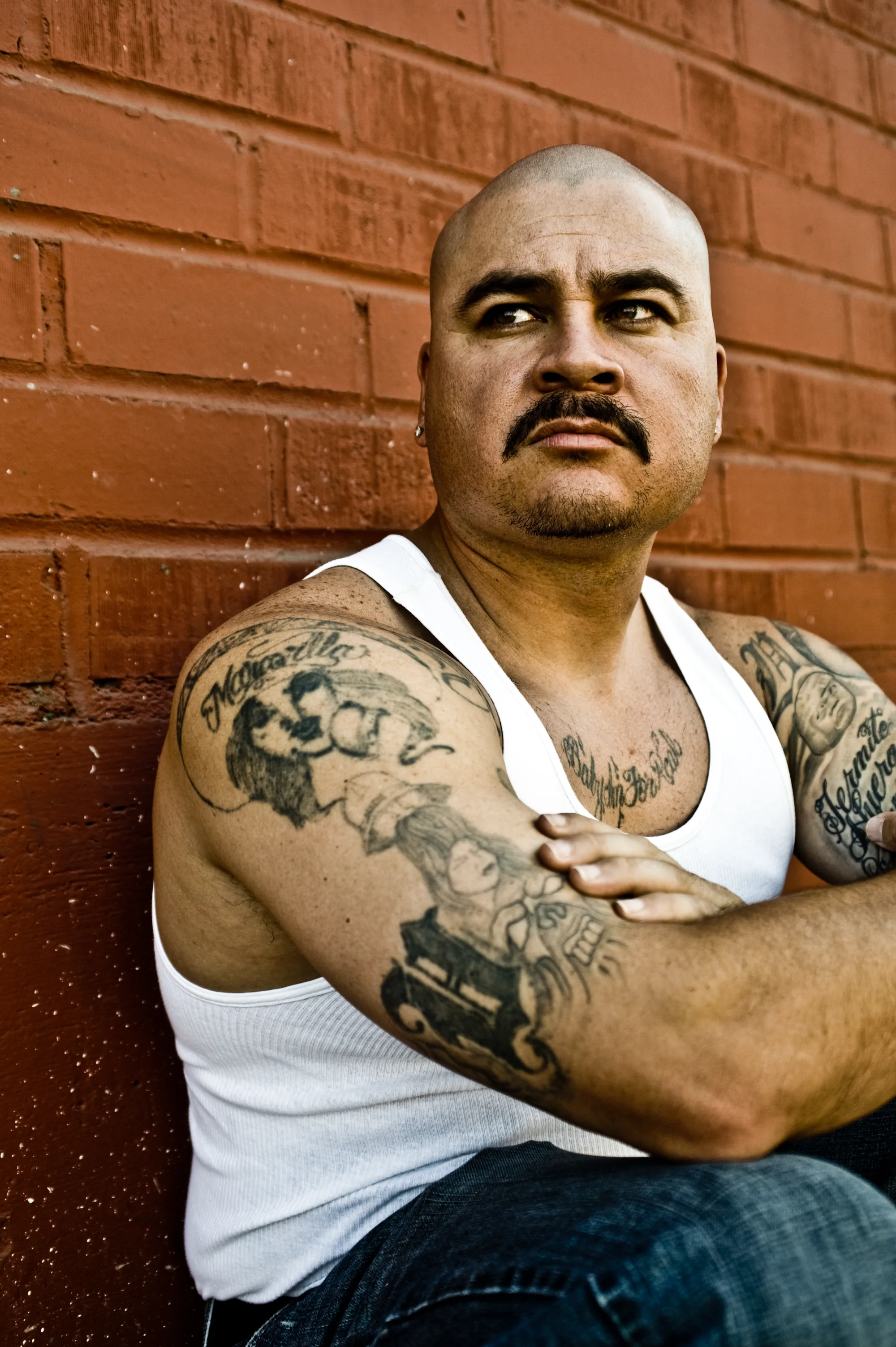 Tattooed artist leaning against a red brick wall in East Los Angeles — Suspect Entertainment, music portrait photography by Janina Laszlo