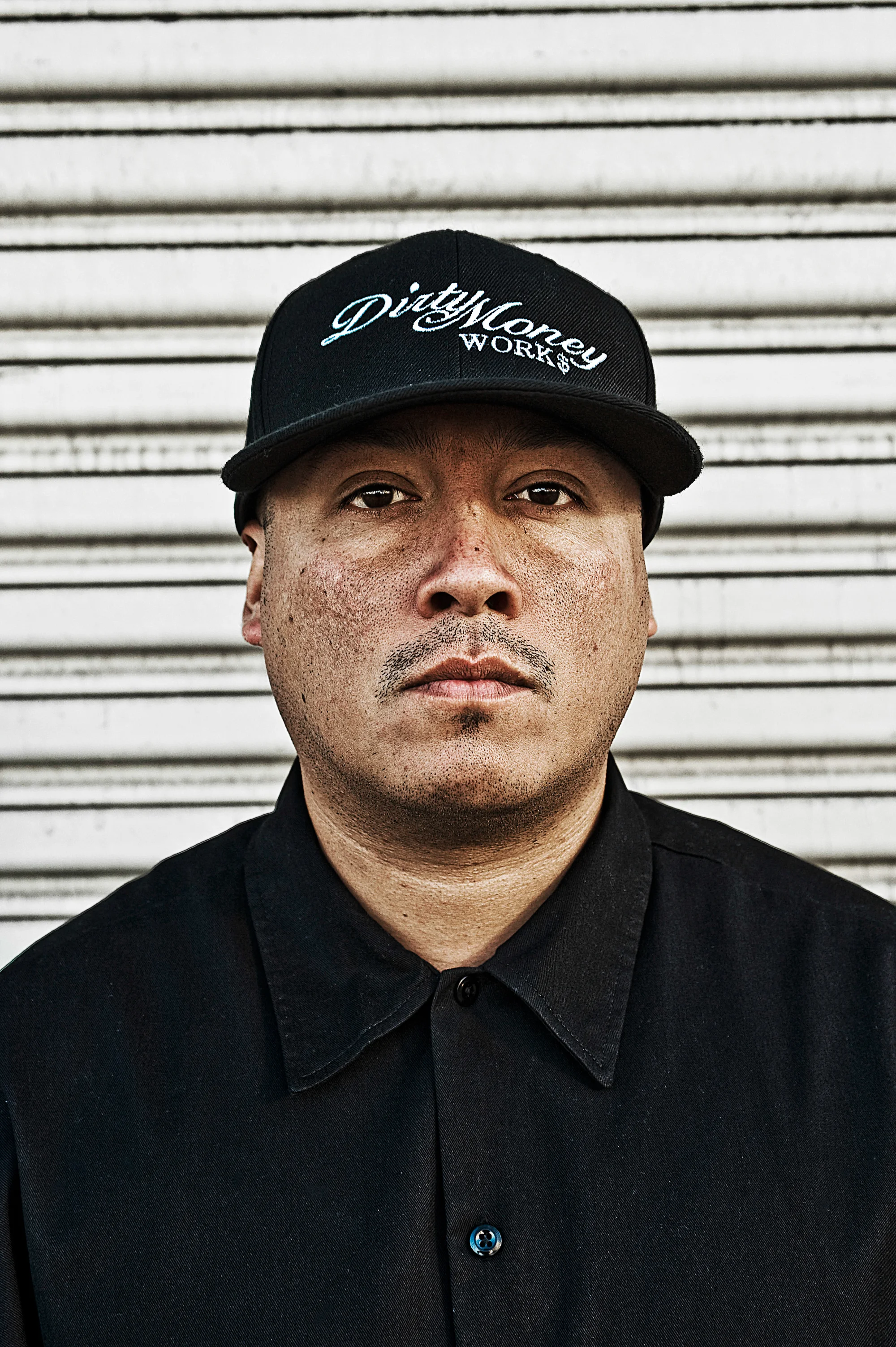Portrait of an artist in a black cap against a metal shutter in East Los Angeles — Suspect Entertainment, music portrait photography by Janina Laszlo