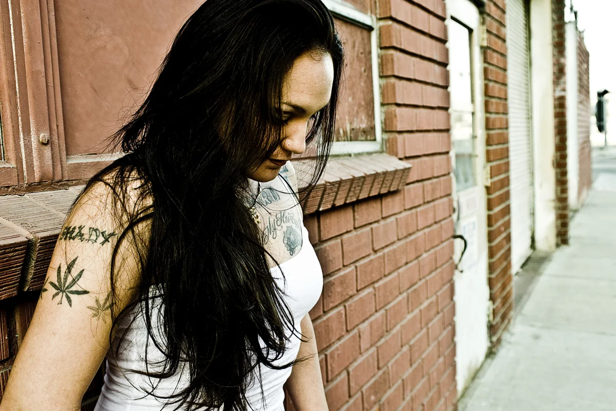 Woman with tattoos leaning on a brick wall, looking down in East Los Angeles — Suspect Entertainment, music portrait photography by Janina Laszlo