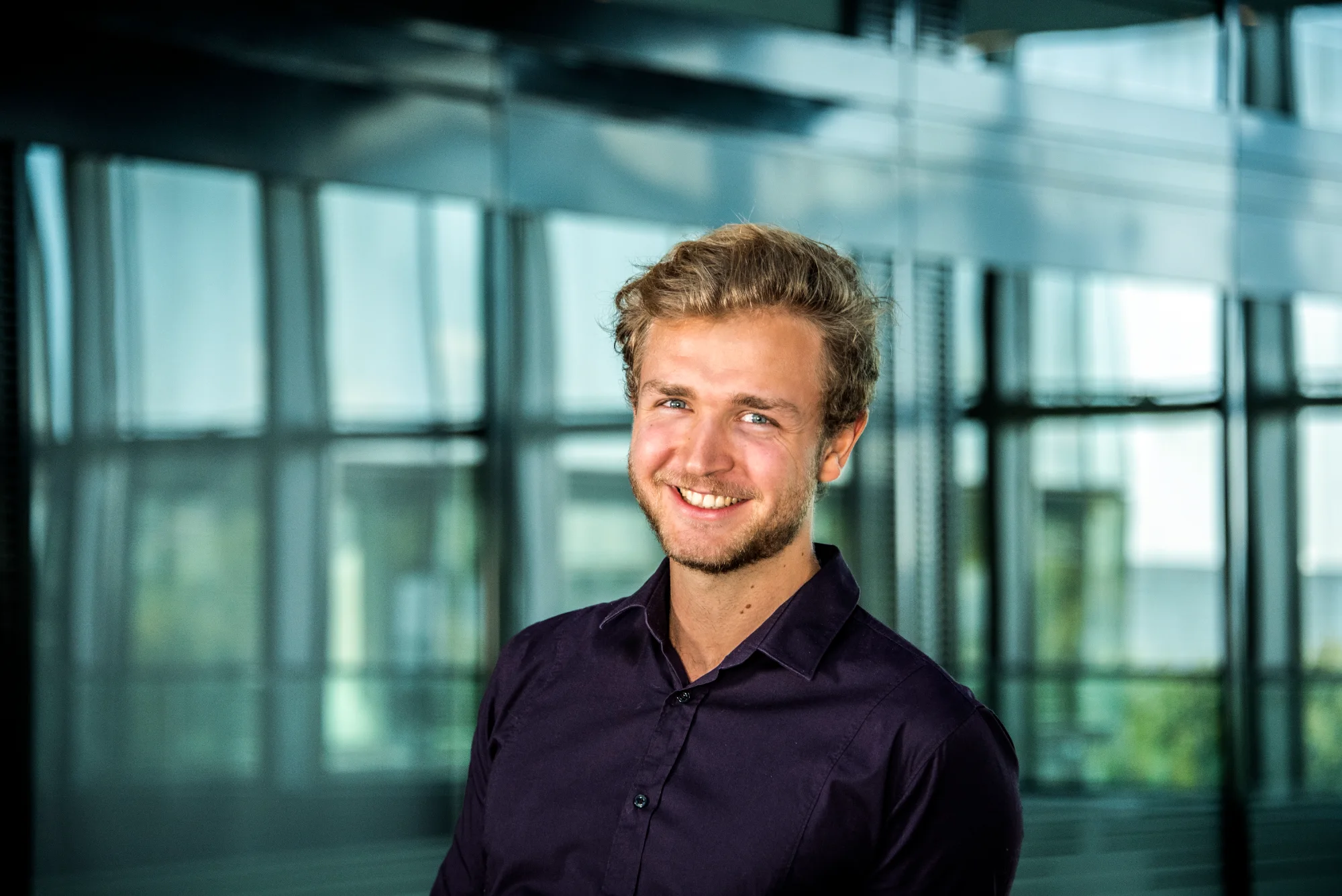 Young man in a dark shirt in the office atrium — SWMH, employer branding photography by Janina Laszlo