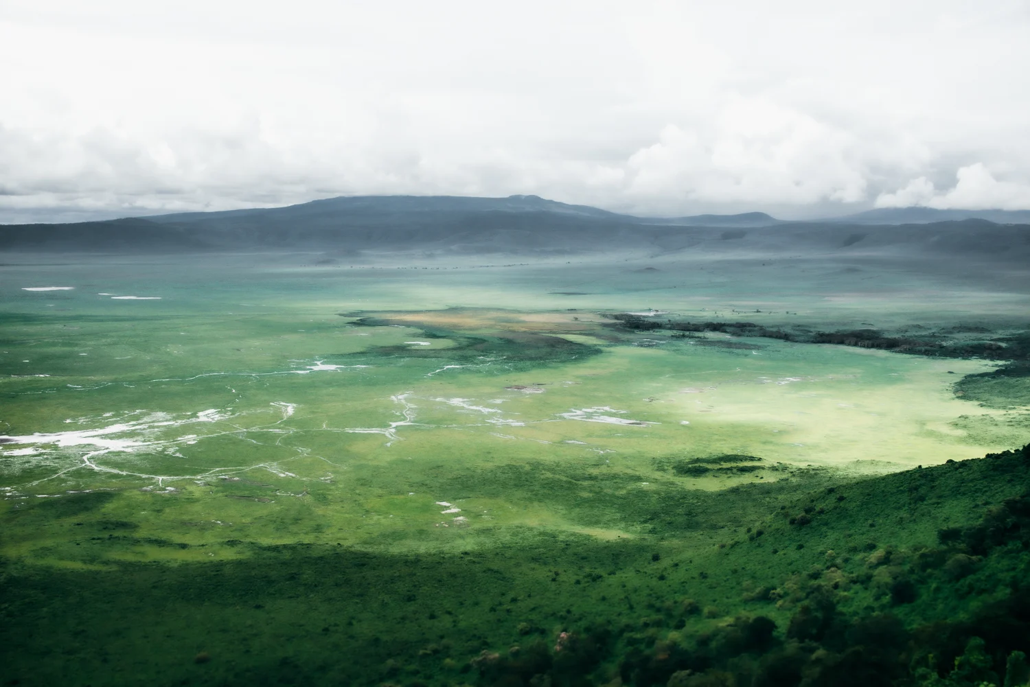 View from the rim into the green Ngorongoro Crater with seasonal lakes and drifting cloud, Ngorongoro Conservation Area — Tanzania, travel and wildlife photography by Janina Laszlo