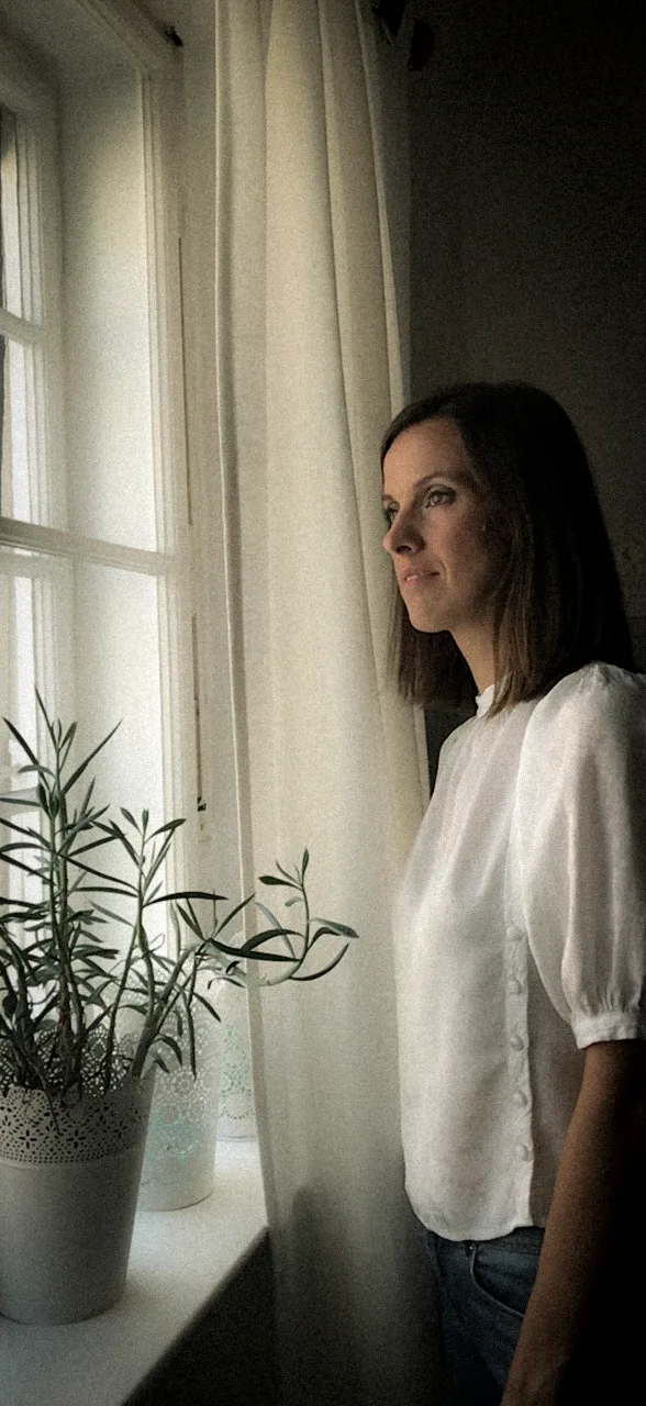 Anja Mörk in a white blouse looking out of a window beside a potted plant, Munich — Deutsche Telekom FaceTime Session, commercial and lifestyle photography by Janina Laszlo