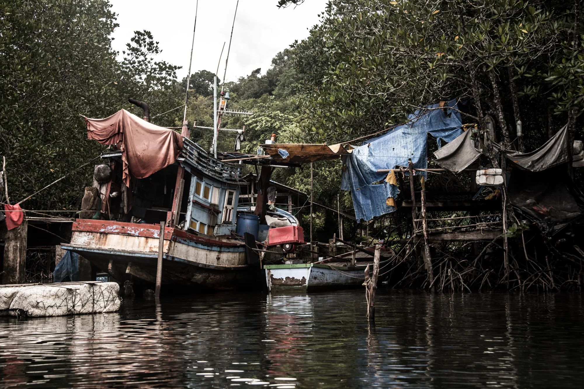 Weathered fishing boat and tarpaulin shelters among mangroves — Thailand, travel and documentary photography by Janina Laszlo