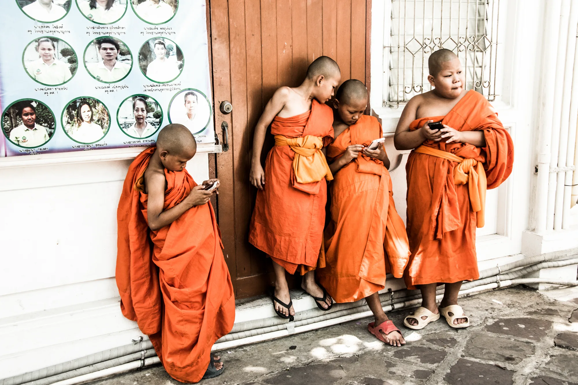 Four young novice monks in saffron robes looking at their phones, Bangkok — Thailand, travel and documentary photography by Janina Laszlo