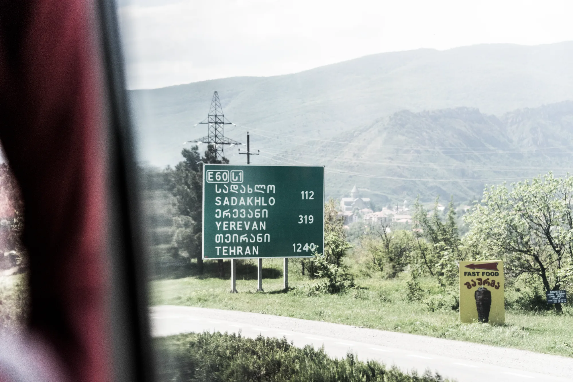 E60 road sign to Sadakhlo, Yerevan and Tehran seen through a bus window near Mtskheta, Georgia — Travel Notes, travel photography by Janina Laszlo