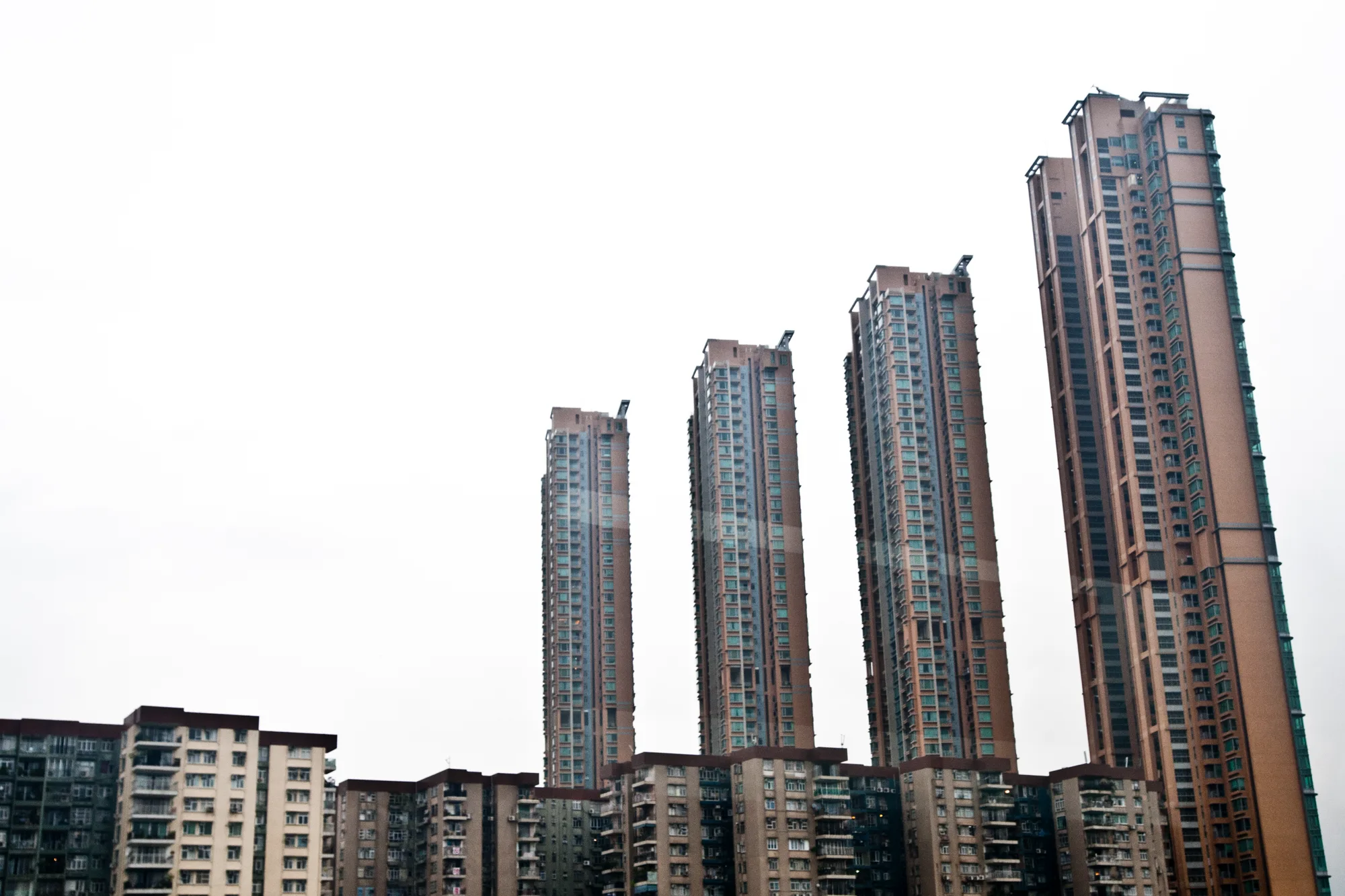 Residential towers rising above older apartment blocks under a white sky, Hong Kong — Travel Notes, travel photography by Janina Laszlo