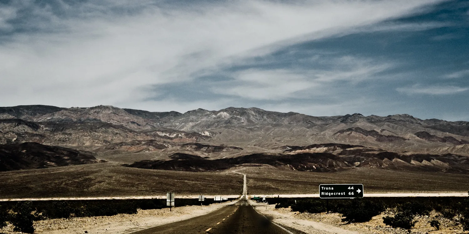 Desert highway into the mountains with a sign to Trona and Ridgecrest, Death Valley region, California — US West Coast, panoramic fine art landscape photography by Janina Laszlo