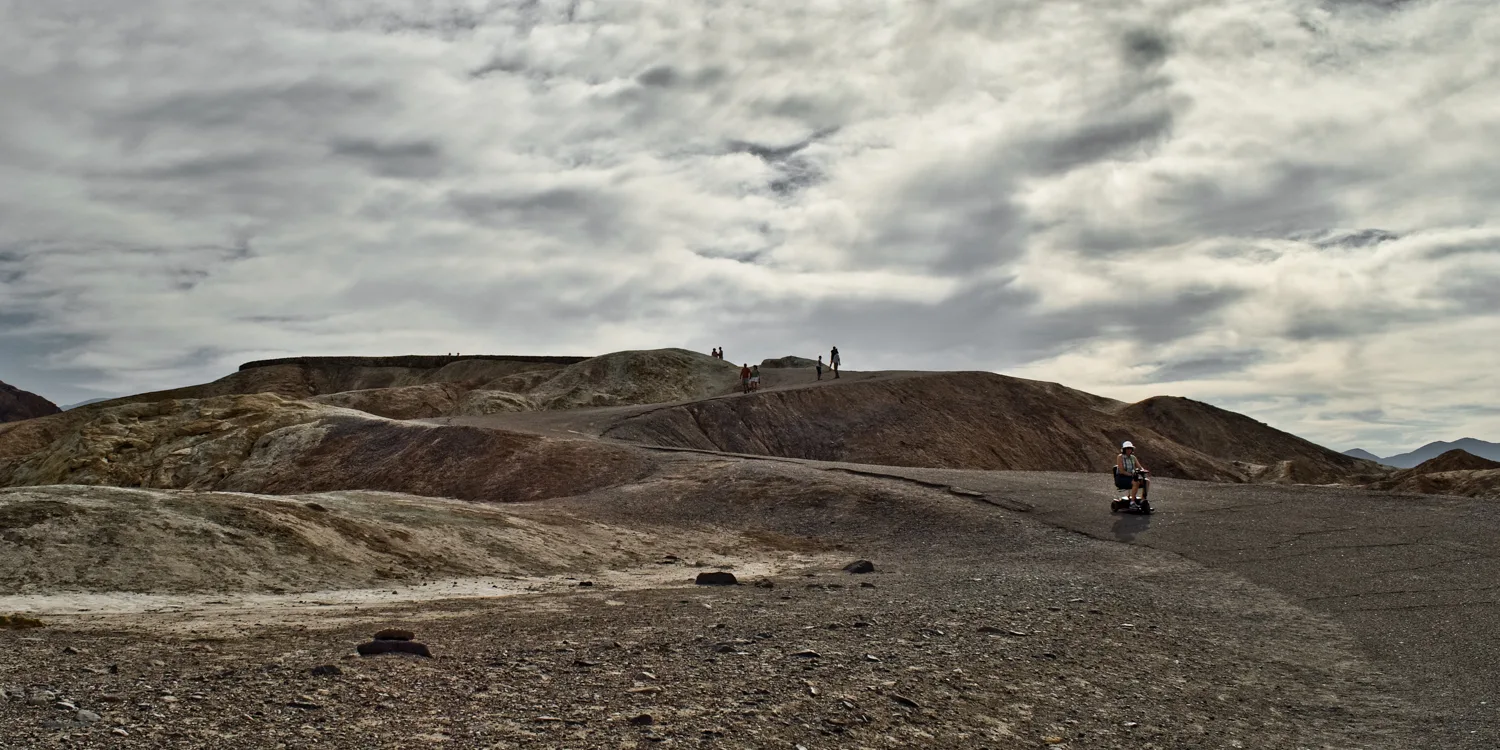 Visitors walking the ridge at Zabriskie Point under heavy clouds, Death Valley National Park — US West Coast, panoramic fine art landscape photography by Janina Laszlo