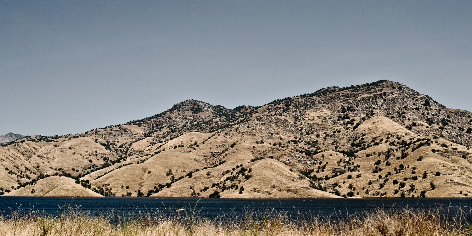 Golden oak-dotted hills above a dark lake in the Sierra foothills, California — US West Coast, panoramic fine art landscape photography by Janina Laszlo