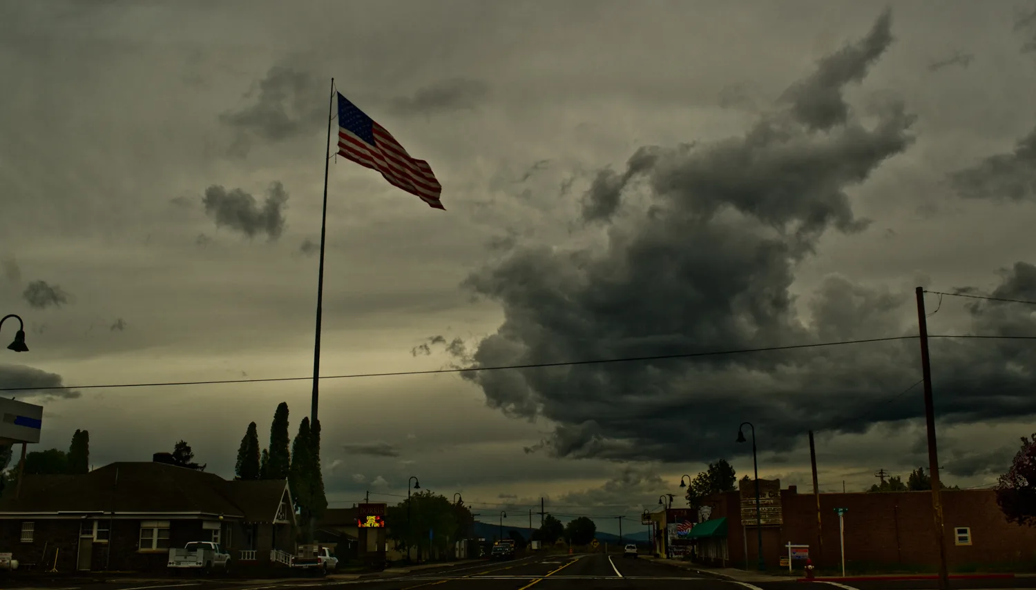 Giant US flag over the main street of a small town under storm clouds, Dorris, California — US West Coast, panoramic fine art landscape photography by Janina Laszlo