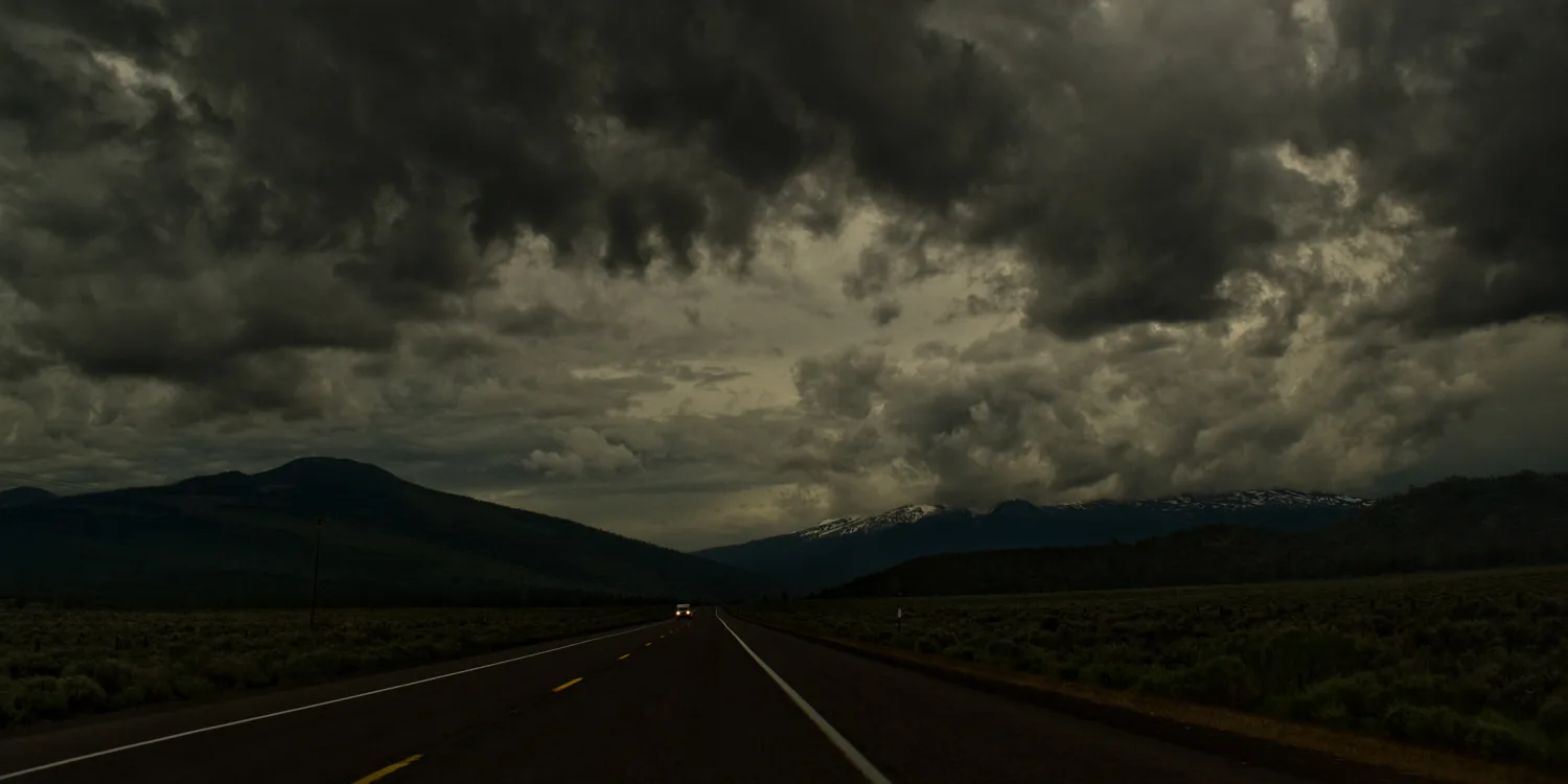 Empty highway toward snow-capped mountains under dark storm clouds, Northern California — US West Coast, panoramic fine art landscape photography by Janina Laszlo